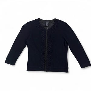 May include: A navy blue zip-up cardigan with long sleeves. The cardigan features a beaded design along the zipper and neckline. The brand tag is visible at the neckline. The garment is displayed on a white background.