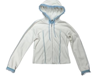 May include: A white zip-up hoodie featuring light blue faux fur trim along the hood edge and sleeve cuffs. The garment includes a full-length front zipper, a drawstring hood, and vertical light blue piping details running down the front and sleeves.
