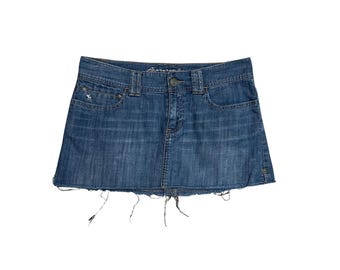 May include: A blue denim mini skirt with a frayed hem. The skirt has a classic five-pocket design, a button and zipper closure, and the brand name "Abercrombie" embroidered on the back. A small embroidered logo is visible on the front pocket.