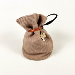 May include: A brown crocheted drawstring bag with a black handle and an orange plastic ring. The bag has a small brown tag attached to it that says "Good Luck".
