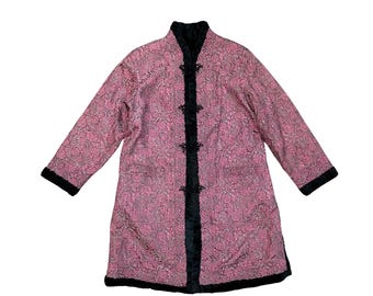May include: A pink floral patterned coat with black trim and frog closures. The coat has long sleeves and a black collar. The coat is made of a soft, textured fabric and has a vintage aesthetic.
