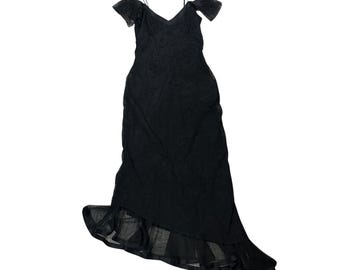 May include: A black, floor-length dress with a V-neckline and spaghetti straps. The dress features off-the-shoulder sleeves and a layered, asymmetrical hemline. The fabric appears to have a subtle floral pattern.