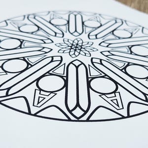 Op de afbeelding: Zwart-wit mandala-ontwerp op wit papier. Het cirkelvormige patroon bevat geometrische vormen, waaronder langwerpige rechthoeken, cirkels en driehoeken, die uitstralen vanuit een centraal bloemmotief. Geschikt om in te kleuren of voor decoratieve doeleinden.