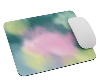 May include: A rectangular mousepad with a watercolor design in shades of pink, green, and yellow. A white wireless mouse is positioned on the right side of the mousepad. The mousepad has a black border.