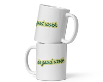 May include: Two white ceramic mugs stacked on top of each other. Each mug has a curved handle and the words "do good work" in a green script font with a yellow outline.