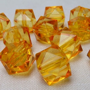 May include: A group of 10 amber glass beads with a faceted, cube-like shape. The beads have a hole in the center for stringing.