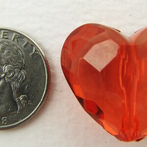 May include: A bright orange heart-shaped bead with a faceted design. The bead is about the size of a US quarter.