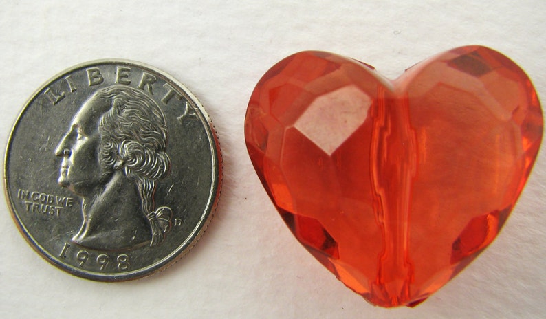 May include: A bright orange heart-shaped bead with a faceted design. The bead is about the size of a US quarter.