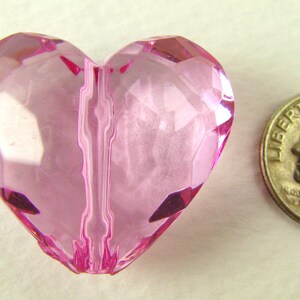 May include: A pink heart-shaped bead with a faceted design. The bead is approximately the size of a US dime.