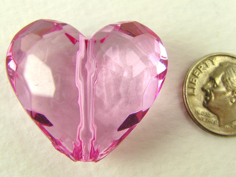 May include: A pink heart-shaped bead with a faceted design. The bead is approximately the size of a US dime.