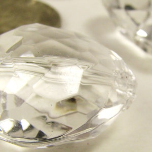 May include: A clear, faceted heart-shaped bead with a slightly cloudy appearance. The bead is made of glass or plastic and has a smooth, polished finish.