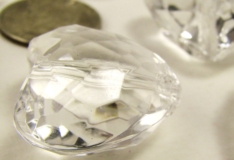 May include: A clear, faceted heart-shaped bead with a slightly cloudy appearance. The bead is made of glass or plastic and has a smooth, polished finish.