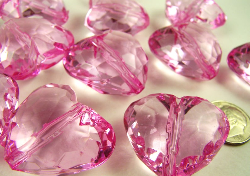 May include: A group of pink heart-shaped glass beads. The beads are faceted and have a hole through the center. They are perfect for making jewelry or other crafts.