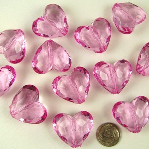 May include: A collection of twelve pink heart-shaped beads. The beads are made of clear acrylic and have a faceted design.