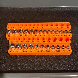 May include: An orange socket organizer with two tiers, holding various sized sockets. The sockets are labeled with both metric and imperial measurements, ranging from 4 to 15 mm and 5/32 to 9/16 inches.
