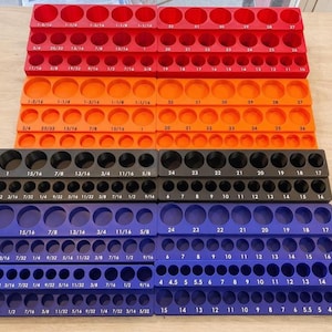 May include: A collection of multi-colored socket organizers. The organizers are red, orange, black, and blue, each with multiple holes for holding sockets. The sizes are printed on each organizer in inches.