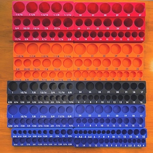 May include: A collection of multi-colored socket organizers. The organizers are in red, orange, black, and blue, each with multiple holes labeled with fractional inch measurements for various socket sizes. The image is taken from a top-down perspective.