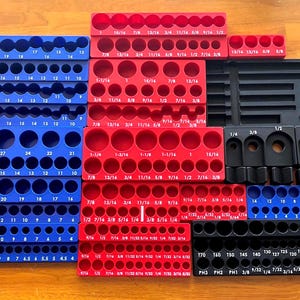 Op de afbeelding: Een verzameling blauwe, rode en zwarte kunststof dopsleutel-organizerbakken met diverse ronde uitsparingen voor gereedschap. Elke bak is voorzien van opgedrukte maataanduidingen in breuken, cijfers of letters voor specifieke organisatie.