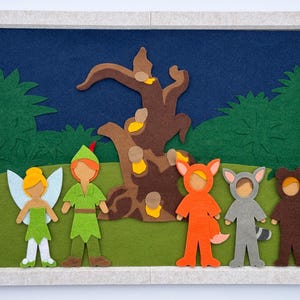 May include: A framed felt art piece depicting a scene with characters. A fairy, Peter Pan, and three costumed figures stand before a tree and green foliage against a dark blue background. The frame is light gray.