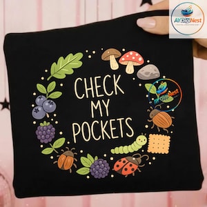 Puede incluir: Bolso tote negro con el texto "CHECK MY POCKETS" rodeado de ilustraciones de setas, bayas, insectos y una galleta. El diseño presenta un tema caprichoso inspirado en la naturaleza con una fuente lúdica.
