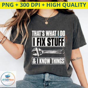 May include: A charcoal gray short-sleeve t-shirt featuring white text that reads THAT'S WHAT I DO I FIX STUFF & I KNOW THINGS, accompanied by a graphic illustration of a silver adjustable wrench centered between the lines of text.
