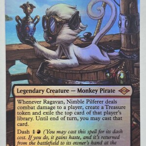 May include: A collectible trading card titled Ragavan, Nimble Pilferer featuring a white monkey wearing goggles, holding a metallic vessel on a wooden ship deck. The card text describes the creature as a Legendary Creature Monkey Pirate.