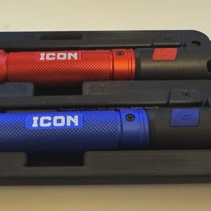 May include: Two flashlights, one red and one blue, are displayed in a black carrying case. The flashlights have the word "ICON" printed on them. The case has a handle and a latch.