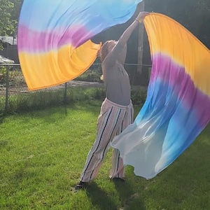 May include: Two large, flowing worship flags made of lightweight fabric featuring a vibrant gradient pattern that transitions from white to blue, purple, and yellow. The flags are held aloft, displaying their expansive, rippling rectangular shape.