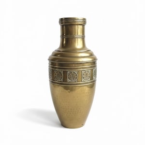 Op de afbeelding: Een messing vaas met een gehamerde textuur en decoratief bladerenpatroon. De vaas heeft een brede basis die taps toeloopt naar een smalle hals. De vaas is ongeveer 30 cm hoog.