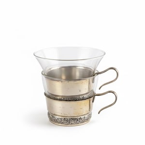 Könnte beinhalten: Zweiteiliges Set aus Vintage-Teetassen. Jede Tasse hat eine klare Glasschale, die in einem silberfarbenen Metallhalter mit Griff eingesetzt ist. Der untere Halter hat ein verziertes Blumendesign. Die Tassen sind übereinander gestapelt.
