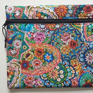 May include: A rectangular zippered pouch with a vibrant floral mosaic pattern. The design features colorful flowers in shades of pink, orange, blue, and green, set against a dark blue background. A wooden button is visible on the top right corner.