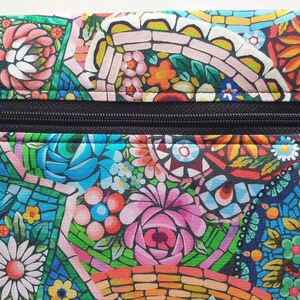 May include: A colorful floral patterned pouch with a black zipper. The design features a mosaic-like arrangement of flowers in shades of pink, blue, orange, and white. The pouch is likely made of fabric.