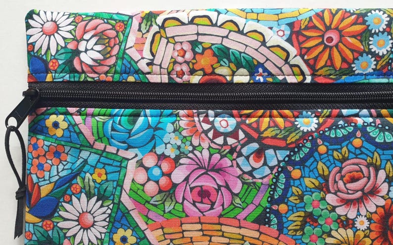 May include: A colorful floral patterned pouch with a black zipper. The design features a mosaic-like arrangement of flowers in shades of pink, blue, orange, and white. The pouch is likely made of fabric.
