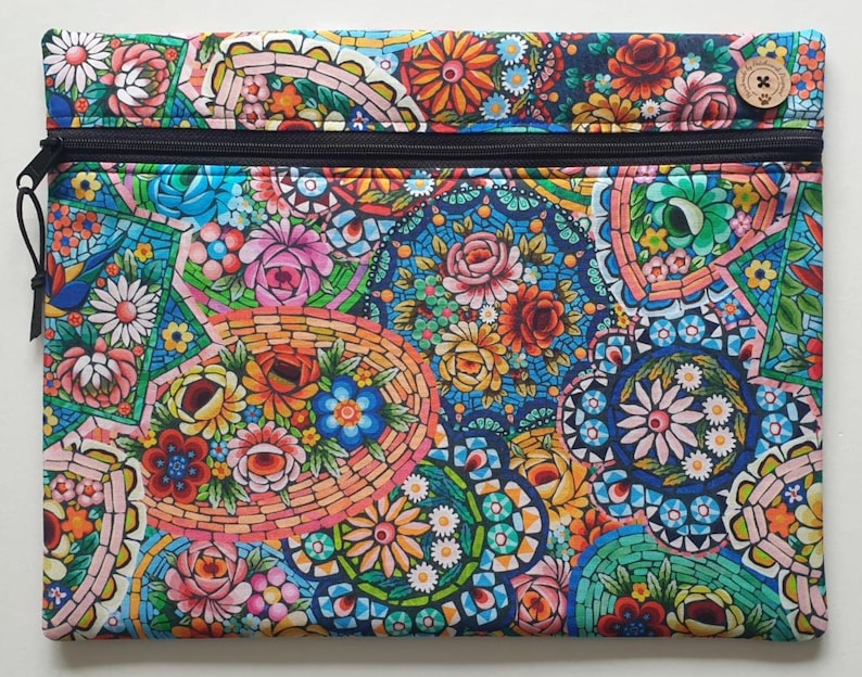 May include: A rectangular zippered pouch with a vibrant floral mosaic pattern. The design features a variety of colorful flowers in shades of pink, orange, blue, and green. A wooden button with a cross design is on the top right corner.