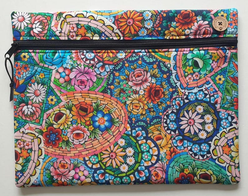 May include: A rectangular zippered pouch with a vibrant floral mosaic pattern. The design features colorful flowers in shades of pink, orange, blue, and green, set against a dark blue background. A wooden button is visible on the top right corner.