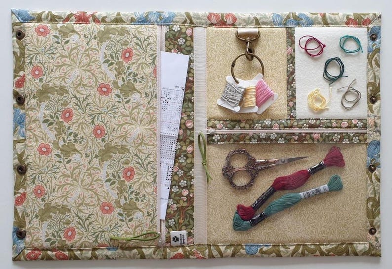 Pode incluir: Um organizador de artesanato em tecido com estampa floral de flores rosas e folhagem verde. Inclui um bolso com z&iacute;per, um anel de metal com tr&ecirc;s carret&eacute;is de linha, uma se&ccedil;&atilde;o de feltro branco, tesoura e duas meadas de linha de bordar.