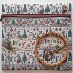 Op de afbeelding: Een vierkant stoffen tasje met ritssluiting, voorzien van een kerstprint met bomen, huisjes en ornamenten. Een houten borduurring en een bewerkte metalen schaar liggen op de voorzijde, waarop de tekst It's the Most Wonderful Time of the Year staat.
