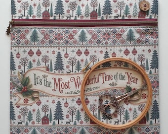 Puede incluir: Una bolsa de tela cuadrada con cierre de cremallera, con un estampado navideño de árboles, casas y adornos. Un bastidor de bordado de madera y unas tijeras de metal ornamentadas se sitúan sobre el texto It's the Most Wonderful Time of the Year.