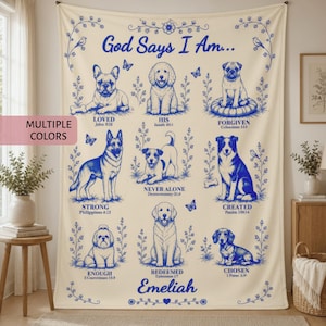 May include: A cream-colored fleece blanket featuring blue line-art illustrations of nine different dog breeds arranged in a grid. The text reads God Says I Am followed by various dog-themed affirmations and scripture references, ending with the name Emeliah.