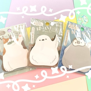 Könnte beinhalten: Drei tierförmige Haftnotizen in Klarsichtverpackung. Die Notizen sind in Form einer Katze, eines Vogels und eines Pinguins gehalten. Die Katze ist weiß und orange, der Vogel ist weiß und der Pinguin ist grau. Jede Packung hat japanischen Text.