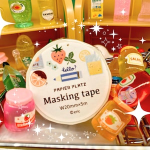 May include: A miniature shopping cart filled with various small, colorful items. A roll of masking tape with fruit illustrations and the text "Masking tape" is in the center. Other items include small jars, bottles, and a red pepper.