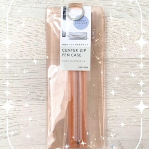Op de afbeelding: Een doorzichtige, perzikroze Center Zip etui met bijpassende rits. De etui heeft een metalen ring aan de bovenkant en een label met Japanse tekst. De tekst "CENTER ZIP PEN CASE" staat erop.