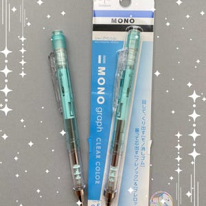 Op de afbeelding: Twee Tombow MONO graph vulpotloden met doorzichtige, lichtblauwe behuizingen. Eén potlood ligt los en de andere zit in de originele blauw-witte verpakking. De verpakking bevat de tekst MONO graph, 0,5 mm en Japanse karakters.