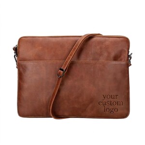 May include: A brown leather laptop bag with a rectangular shape, a front pocket, and an adjustable shoulder strap. The bottom right corner features the embossed text "your custom logo" in a simple, clean, sans-serif font style.