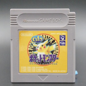 May include: A gray Game Boy Color cartridge with a yellow label featuring Pikachu, the text "Pocket Monsters", and the Japanese text "ポケットモンスター". The label also includes the text "Nintendo Game Boy" and "DMG-APSJ-JPN".