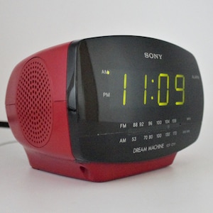 May include: A red Sony Dream Machine clock radio with a digital display showing 11:09. The radio has a speaker on the left side and a dial for tuning AM and FM frequencies.