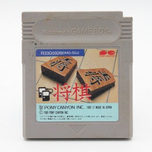 May include: A gray Nintendo Game Boy cartridge featuring the game "Shogi." The label displays two brown game pieces with Japanese characters. The cartridge has the text "Pony Canyon Inc. 1989 12 Made in Japan."