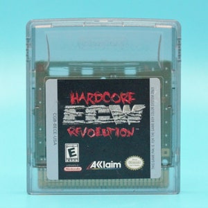 May include: A Game Boy Color game cartridge for Hardcore  ECW Revolution. The cartridge is gray and has a black label with white text. The label says "CGB-BECE-USA" and "Hardcore ECW Revolution". The label also has a red "E" for "Everyone" rating from the ESRB.