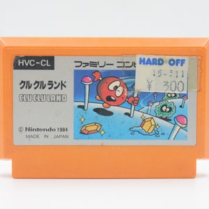 May include: A vintage orange Nintendo Entertainment System (NES) game cartridge for the game "クルクルランド" (Clu Clu Land). The cartridge has a label with Japanese text and a red character on a blue background. The label also includes the text "HVC-CL" and "Nintendo 1984".