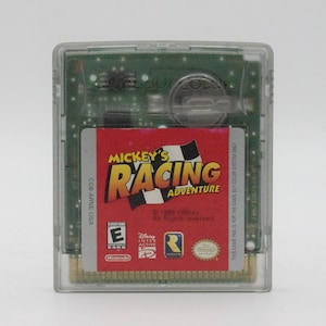 May include: A clear plastic Game Boy Color cartridge case with a red label. The label features the text "MICKEY'S RACING ADVENTURE" in white and yellow lettering. The label also includes the text "CGB-ARNE-USA" and an "E" for "Everyone" rating from the ESRB.